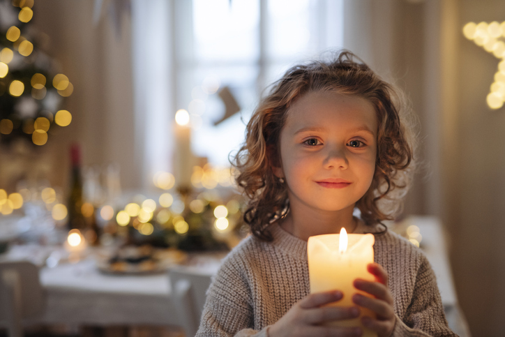 Front view of cheerful small girl holding candle.