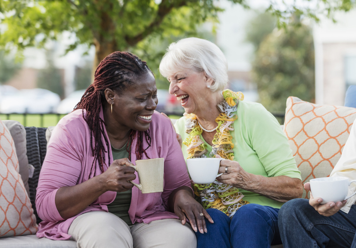 Two older women laughing and enjoying a cup of coffee together outside
