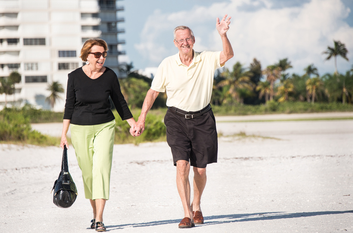 A senior man and a senior woman walking on a beach and holding hands