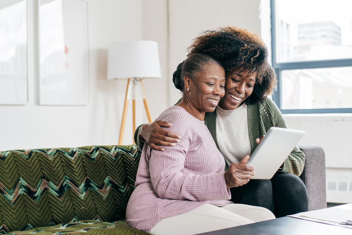 Senior woman and adult daughter looking at tablet and smiling.