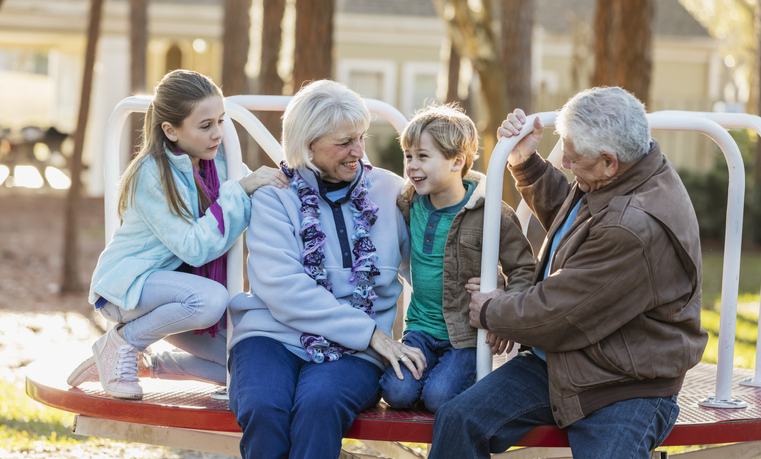 Two children at a playground with their grandparents, sitting on a merry-go-round