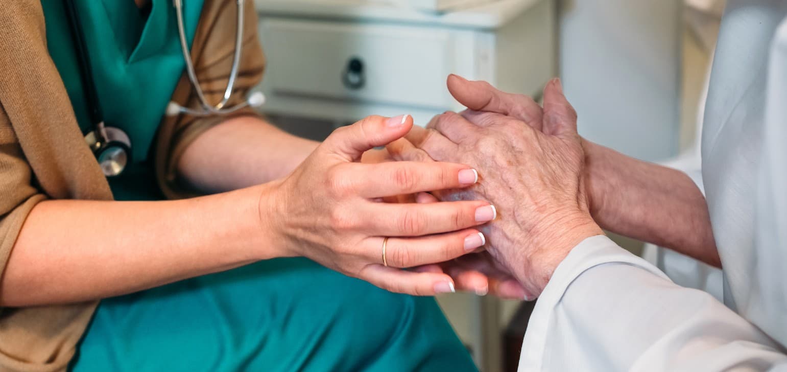 Elderly hands holding the hands of younger medical professional.