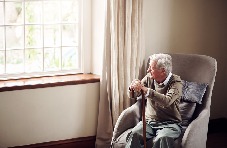 Older adult man sitting in a chair and looking out the window