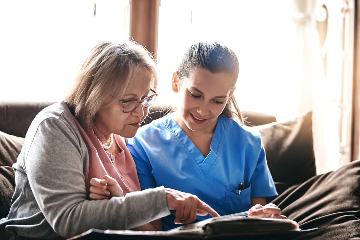 Shot of a nurse and a senior woman looking at a photo album together.