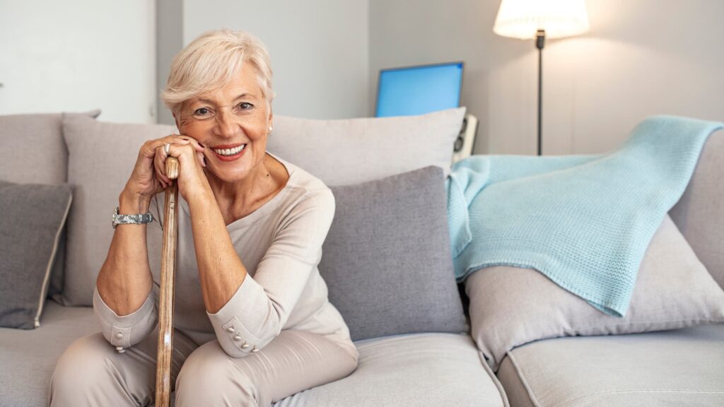 Happy older woman sitting on a couch and resting on a cane.
