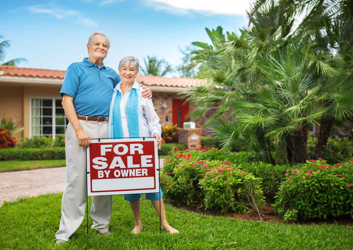 Older adult couple with home for sale sign