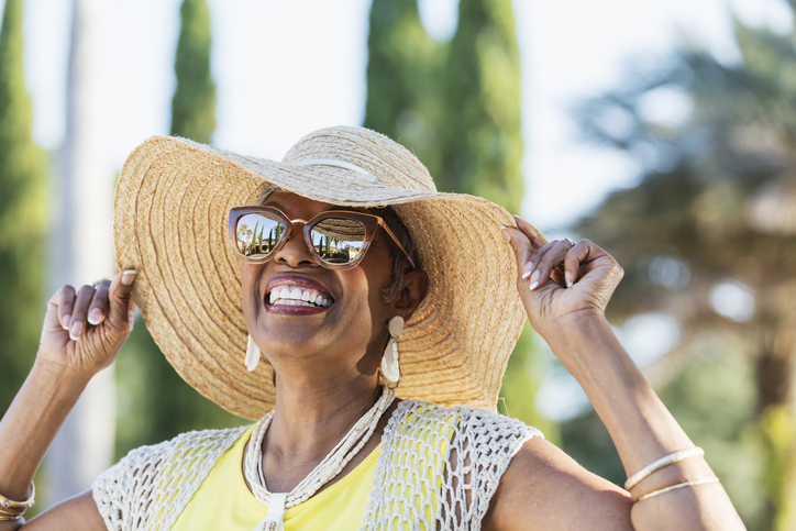 senior woman enjoying a sunny day with a large beach hat and big sunglasses, grinning widely